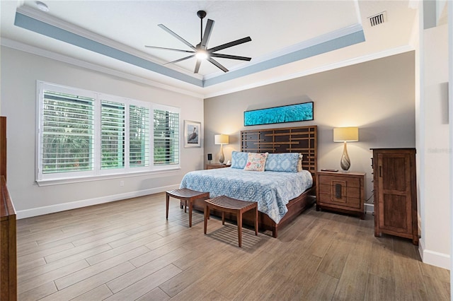 bedroom featuring hardwood / wood-style flooring, ceiling fan, ornamental molding, and a raised ceiling