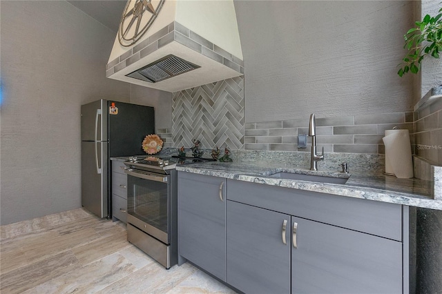 kitchen featuring wall chimney range hood, sink, gray cabinets, backsplash, and stainless steel appliances