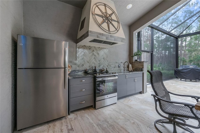 kitchen with dark stone countertops, appliances with stainless steel finishes, gray cabinets, custom range hood, and a high ceiling