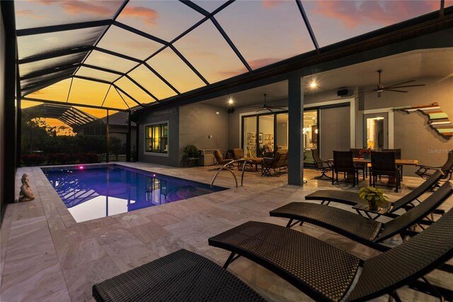 pool at dusk featuring a patio, ceiling fan, and glass enclosure