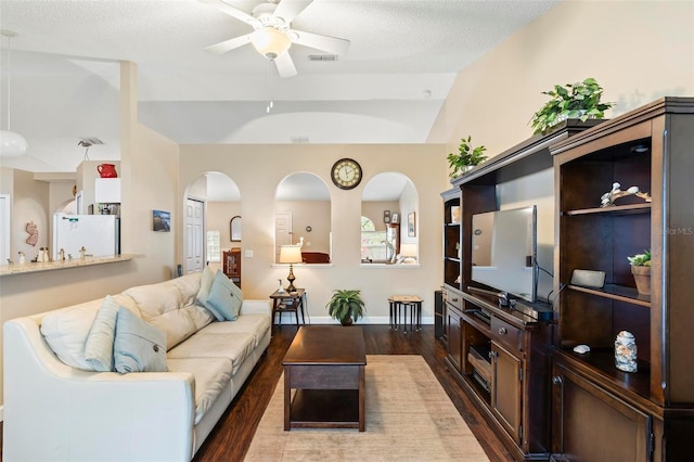 living room with ceiling fan, a textured ceiling, dark hardwood / wood-style flooring, and vaulted ceiling