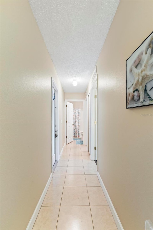 hall with a textured ceiling and light tile patterned floors