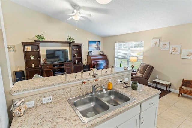 kitchen featuring a textured ceiling, white cabinetry, light tile patterned floors, sink, and lofted ceiling