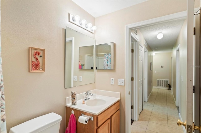 bathroom featuring vanity, toilet, tile patterned floors, and a textured ceiling