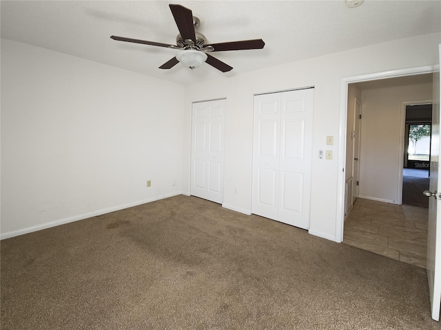 unfurnished bedroom featuring two closets, ceiling fan, and dark colored carpet