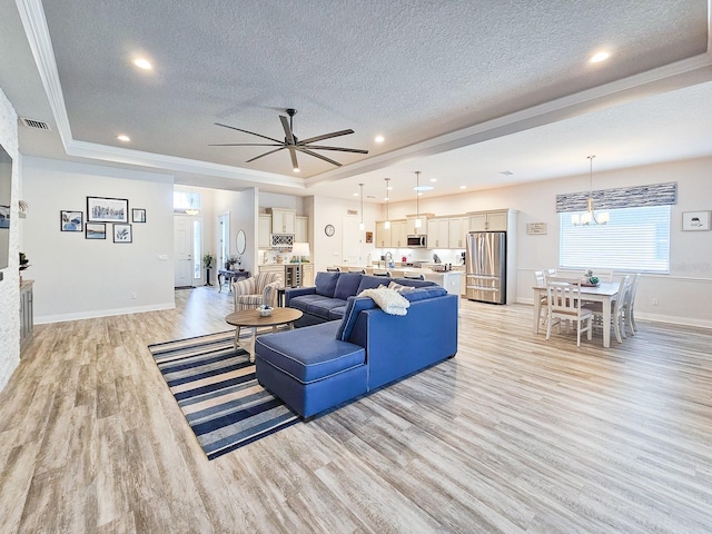 living room featuring a raised ceiling, ceiling fan with notable chandelier, a textured ceiling, and light wood-type flooring