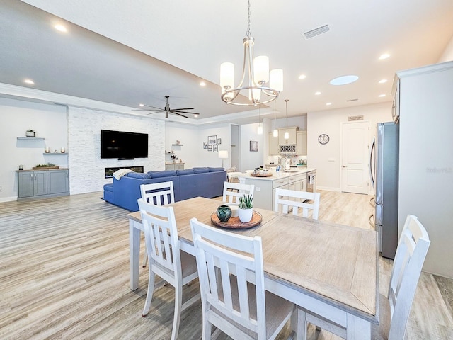 dining space featuring ceiling fan with notable chandelier, ornamental molding, sink, and light hardwood / wood-style flooring