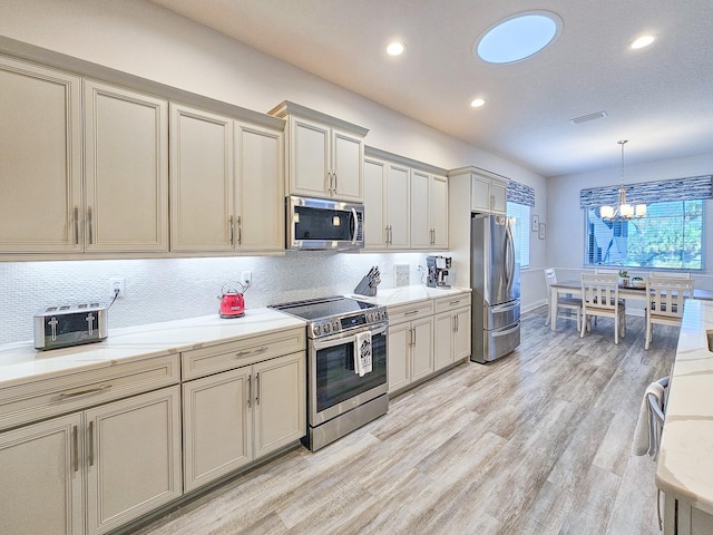 kitchen with pendant lighting, appliances with stainless steel finishes, cream cabinets, and backsplash