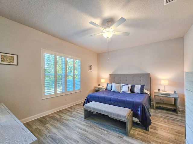 bedroom with ceiling fan, wood-type flooring, and a textured ceiling