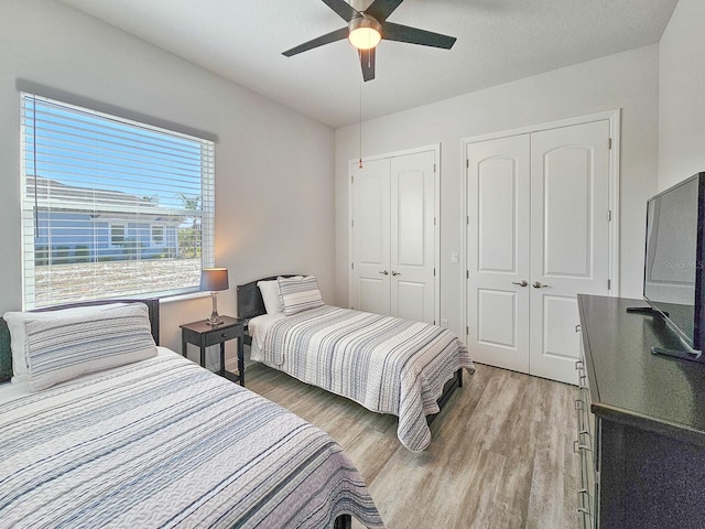 bedroom with multiple closets, wood-type flooring, a textured ceiling, and ceiling fan