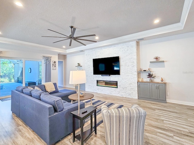 living room featuring a stone fireplace, a textured ceiling, light hardwood / wood-style floors, and a tray ceiling