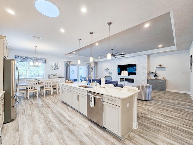 kitchen featuring sink, stainless steel appliances, a raised ceiling, and a center island with sink