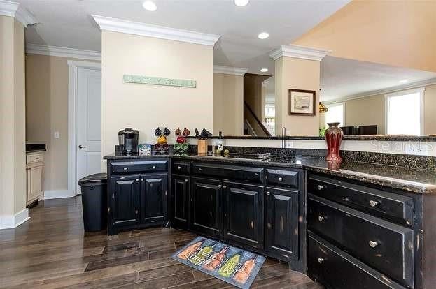 kitchen with kitchen peninsula, dark hardwood / wood-style floors, dark stone counters, and ornamental molding