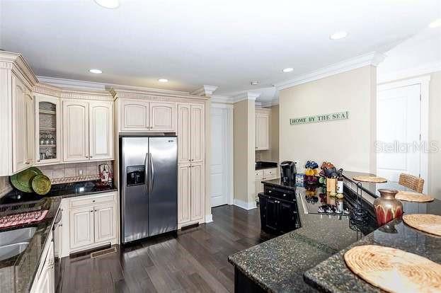 kitchen featuring dark stone countertops, ornamental molding, dark wood-type flooring, backsplash, and stainless steel fridge