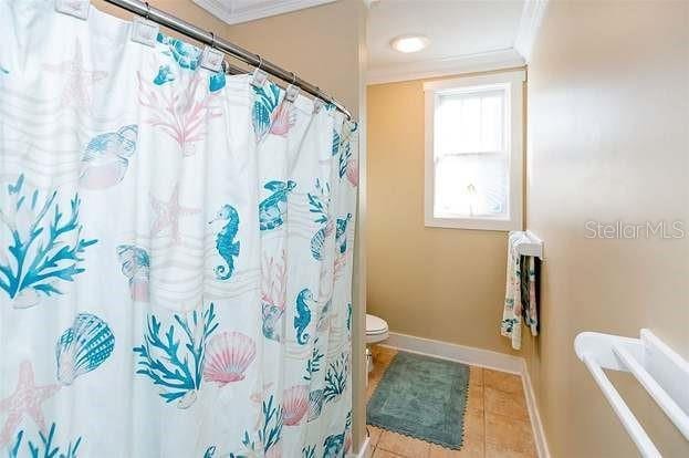 bathroom featuring tile patterned floors, toilet, ornamental molding, and curtained shower