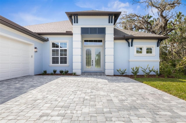 view of front of home with french doors, decorative driveway, stucco siding, a shingled roof, and a garage