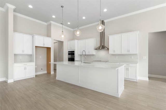 kitchen with light countertops, a sink, wall chimney range hood, and white cabinetry