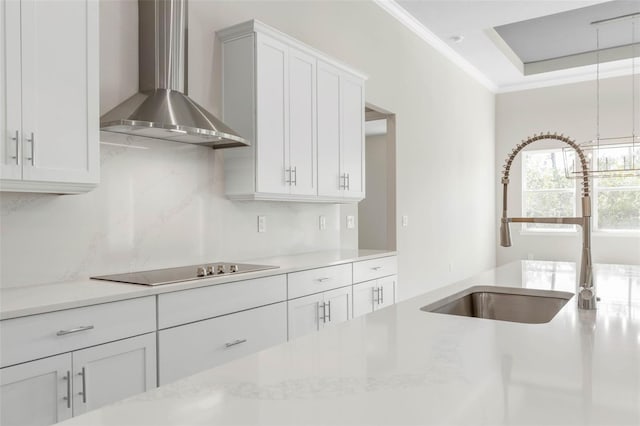 kitchen with black electric cooktop, a sink, white cabinets, wall chimney exhaust hood, and crown molding