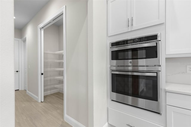 kitchen with baseboards, white cabinets, light countertops, stainless steel double oven, and light wood-style floors