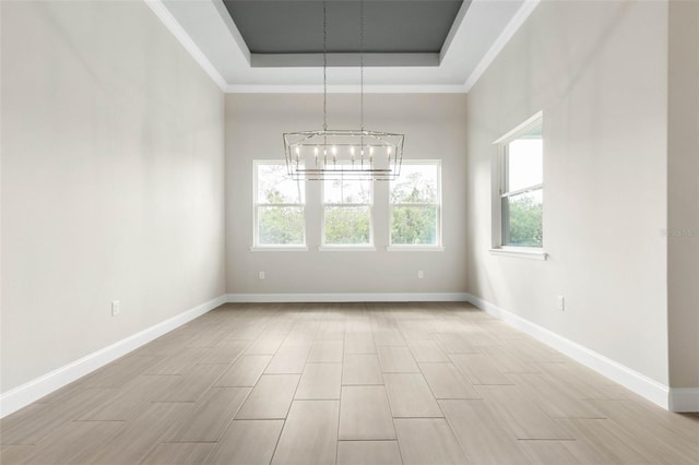 spare room with a chandelier, light wood-style floors, a raised ceiling, and baseboards