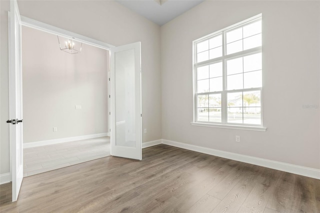 unfurnished room featuring an inviting chandelier, baseboards, and wood finished floors