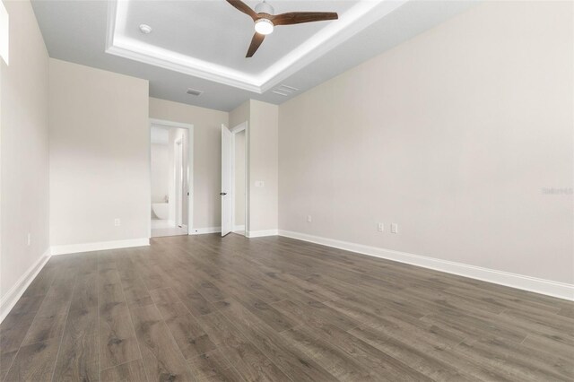 empty room with visible vents, baseboards, a raised ceiling, dark wood finished floors, and ceiling fan