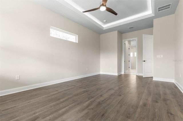 spare room with dark wood-style floors, a raised ceiling, visible vents, and baseboards