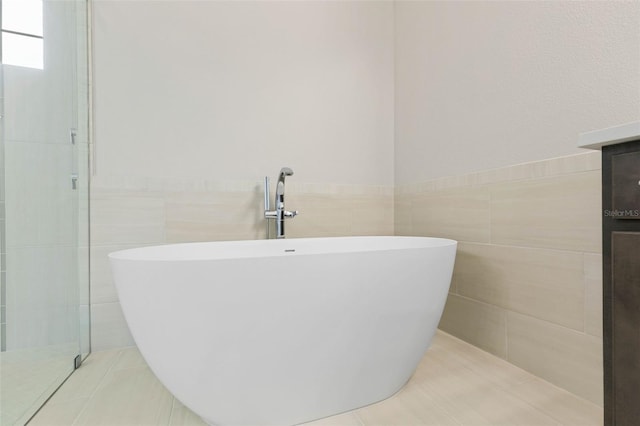 bathroom featuring a wainscoted wall, a soaking tub, tile patterned flooring, and tile walls