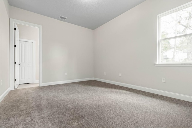 empty room with carpet, visible vents, and baseboards