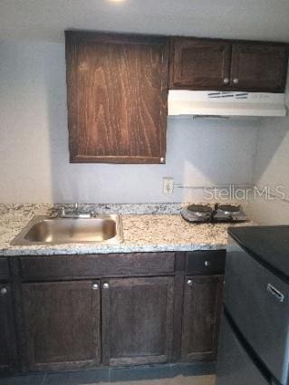 kitchen featuring light stone counters, sink, and dark brown cabinetry