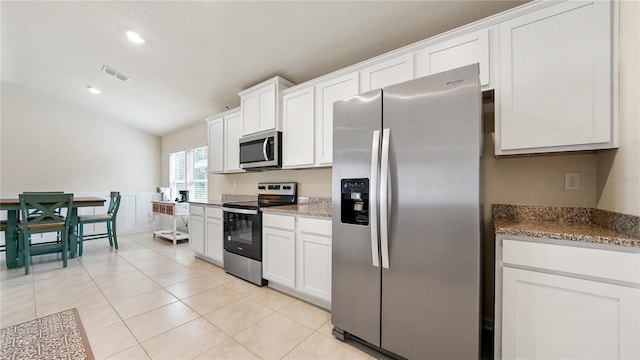 kitchen featuring appliances with stainless steel finishes, lofted ceiling, white cabinetry, stone countertops, and light tile patterned flooring