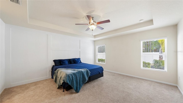 carpeted bedroom featuring ceiling fan, multiple windows, and a raised ceiling