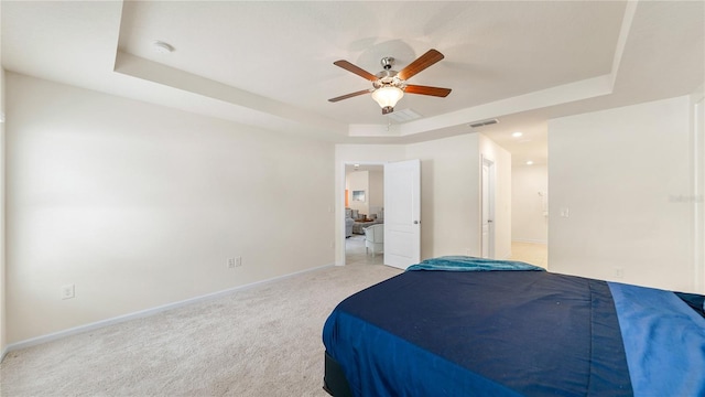 bedroom featuring ceiling fan, light colored carpet, and a tray ceiling