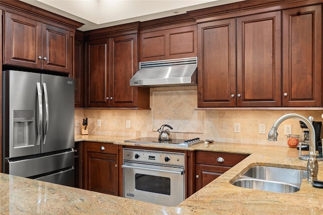 kitchen featuring tasteful backsplash, appliances with stainless steel finishes, light stone counters, range hood, and a sink