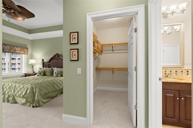 bedroom with light colored carpet, a sink, baseboards, ornamental molding, and a walk in closet