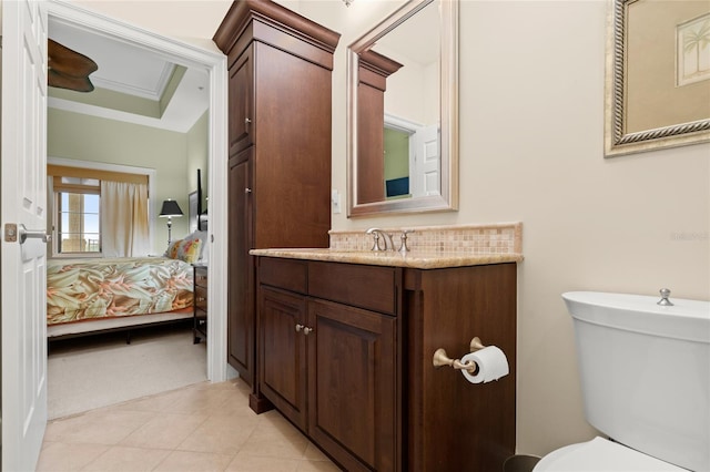 bathroom with a raised ceiling, connected bathroom, toilet, crown molding, and vanity