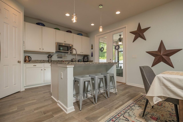 kitchen featuring stone countertops, hanging light fixtures, white cabinetry, a breakfast bar, and an island with sink