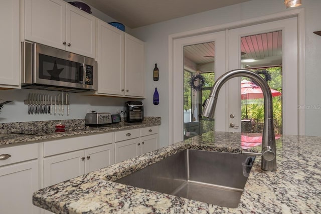 kitchen featuring light stone countertops, sink, white cabinetry, and black electric cooktop