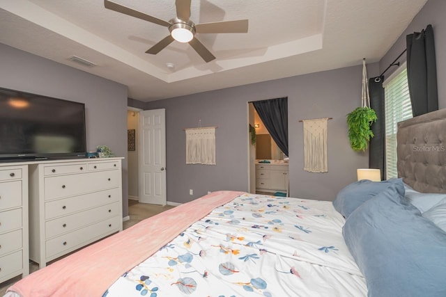 bedroom featuring ensuite bath, ceiling fan, and a raised ceiling