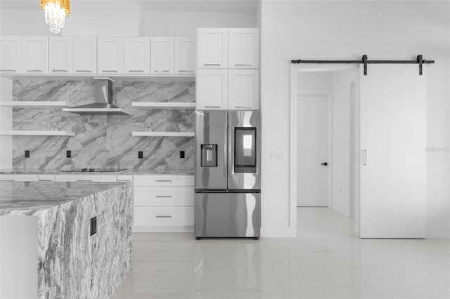 kitchen with white cabinetry, light stone counters, wall chimney exhaust hood, and stainless steel refrigerator with ice dispenser