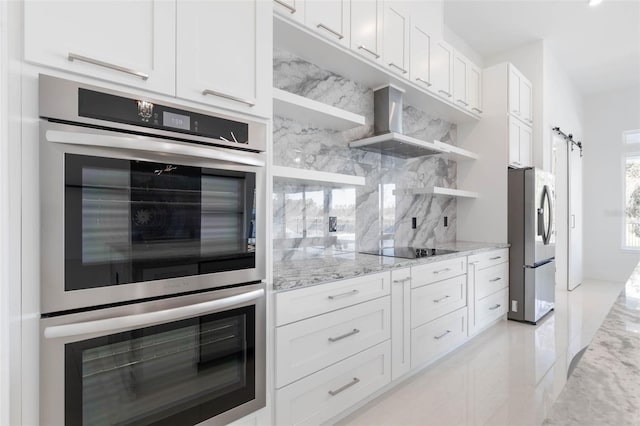 kitchen featuring white cabinetry, stainless steel appliances, a barn door, and wall chimney exhaust hood