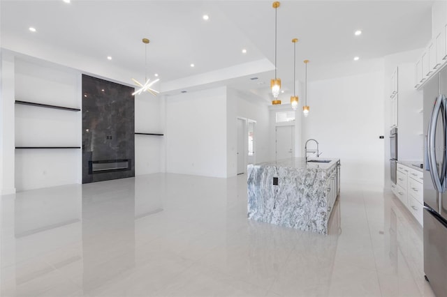 kitchen with hanging light fixtures, light stone countertops, a large island, and white cabinets