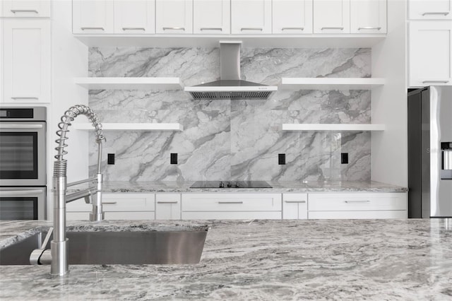 kitchen with wall chimney range hood, sink, stainless steel appliances, light stone countertops, and white cabinets