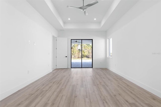 empty room featuring a raised ceiling, ceiling fan, and light hardwood / wood-style floors