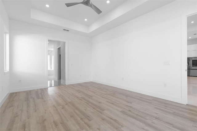 unfurnished room featuring a tray ceiling, ceiling fan, and light wood-type flooring