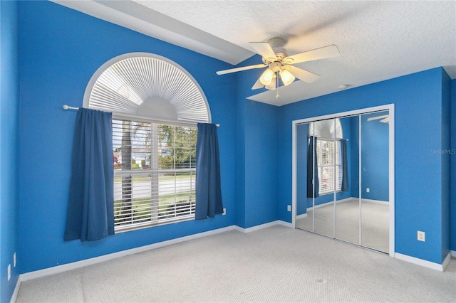 unfurnished bedroom featuring carpet, a textured ceiling, a closet, and ceiling fan