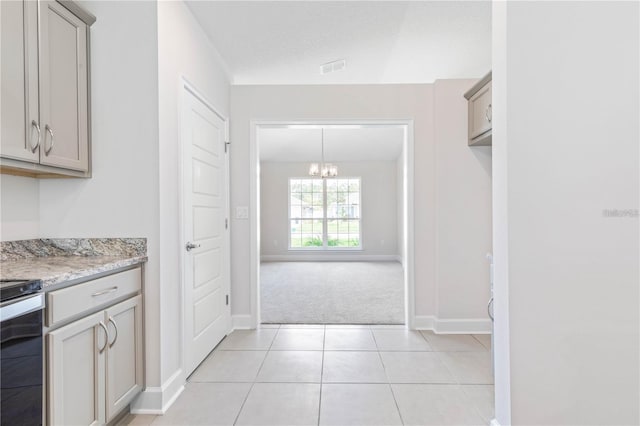 kitchen with light stone countertops, gray cabinets, a chandelier, light colored carpet, and stove