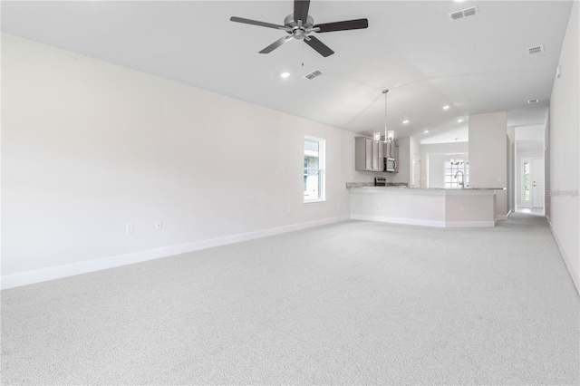 unfurnished living room featuring ceiling fan with notable chandelier, light carpet, and lofted ceiling