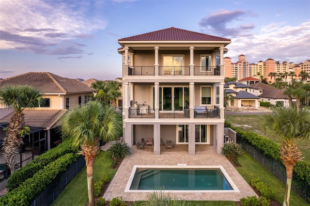 back house at dusk with a swimming pool with hot tub, a balcony, and a patio area