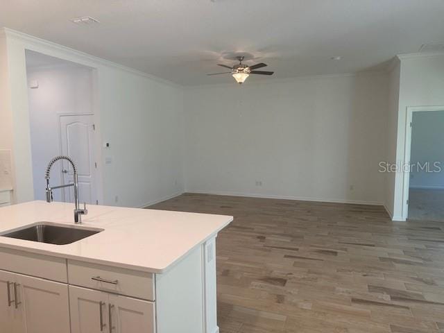 kitchen with sink, white cabinetry, crown molding, wood-type flooring, and a kitchen island with sink